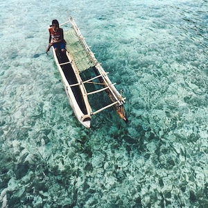 Local Boy in traditional bamboo canoe in clear blue water in Papua New Gunea